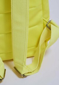 Gul ryggsäck gjord av texturerat tyg, med vadderade remmar och metallbeslag. Remmarna är justerbara och har en robust design.