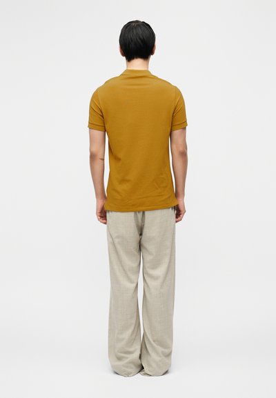 Κίτρινη μουσταρδί κοντομάνικη μπλούζα από απαλό ύφασμα, σε συνδυασμό με ανοιχτό γκρι, φαρδιά παντελόνια, από πίσω.