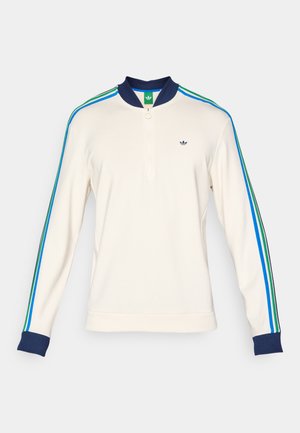 Cream zip-up sweatshirt with navy collar, green label, and vertical stripes in blue, green, and black along the sleeves. Cotton blend fabric.