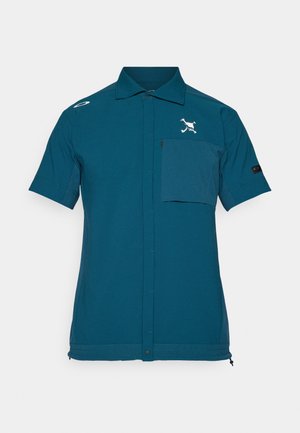 Rövid ujjú, türkiz színű ing sima anyagból, elülső zsebbel, gombos záródással, és logó hímzéssel a mellkasán.