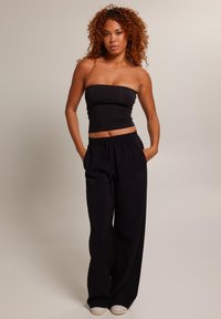 Top noir sans bretelles associé à un pantalon noir ample, avec une taille élastique et des poches latérales, sur fond neutre.