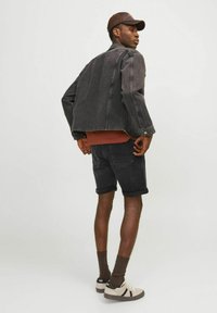 Zwarte denimjas, bruine crew-neck shirt, zwarte shorts en beige sneakers. De jas heeft knoopdetails en een iets cropped pasvorm.