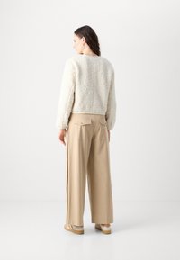 White faux fur jacket with a cropped design and ribbed hem, paired with beige wide-leg trousers featuring back pockets.
