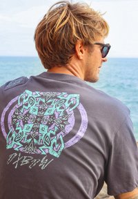 T-shirt en coton gris avec un grand motif géométrique multicolore au dos, agrémenté d'accents turquoise, violet et noir.