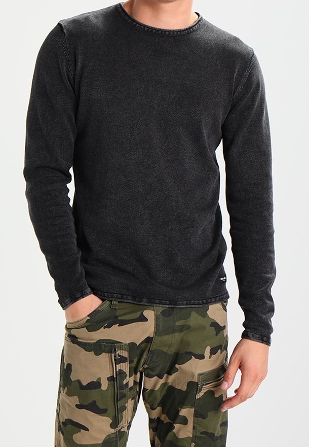 Camiseta negra de manga larga con cuello redondo, con una textura desgastada y costuras visibles, combinada con pantalones cargo de camuflaje.