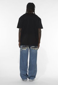 Sort oversized t-shirt og slidte blå jeans med eksponerede lapper og frynset kant, der har en afslappet pasform og sænkede skuldre.
