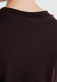 Dark brown, short-sleeve shirt showing smooth texture and minimal stitching details at the collar and shoulder. Classic, simple design.