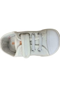 Zapatilla de lona blanca con punta de goma, ojales plateados y correa de velcro. Presenta una parte superior texturizada y una plantilla acolchada.