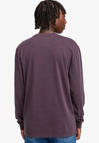 Long-sleeve shirt in dark purple cotton with a relaxed fit, plain back, and rounded neckline, paired with light blue jeans.