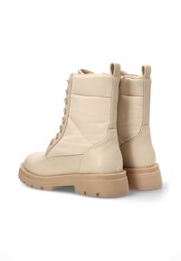 Botas de tobillo de cuero beige con un acabado texturizado, que cuentan con un cierre de cordones en la parte delantera y una suela gruesa marrón. Incluyen lengüetas para ponerlas y quitarlas fácilmente.
