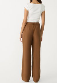 Pantalons larges marron avec une taille élastique, texture lisse et un design fluide, associés à un haut ajusté blanc.