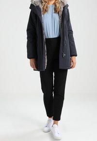 Granatowa ocieplana kurtka z kapturem wyściełanym sztucznym futrem, zapinana na zamek, połączona z jasnobłękitnym topem, czarnymi spodniami i białymi trampkami.