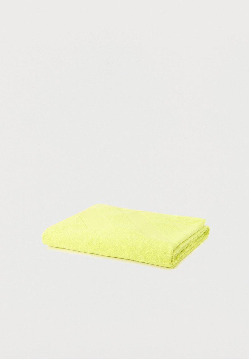 Serviette jaune vif pliée sur un fond gris clair uni, avec une texture visible et des bords nets.