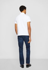 Biała koszulka polo z klasycznym kołnierzykiem, zestawiona z ciemnoniebieskimi dżinsami slim-fit. Materiał wydaje się gładki z minimalnymi detalami.