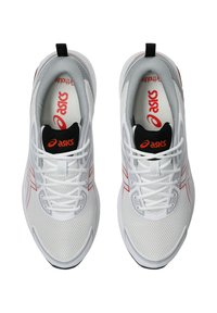 Baskets de sport blanches avec une tige en maille, accents rouges et une languette noire. Elles disposent d'un système de laçage et d'une semelle texturée pour une meilleure adhérence.