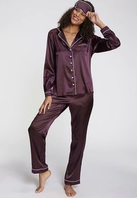Silky burgundy pajama set with white piping, featuring a button-up top with a pocket and long pants. Includes a matching sleep mask.