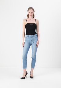 Musthave mustriga tank top õhukeste rihmade ja läbipaistva paneeliga. Heleda sinise kõrge taljega teksapüksid, kitsas lõige, lõpetatud mustade stiletto kontsadega.