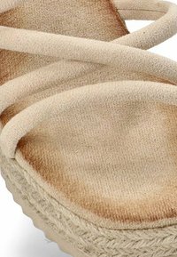 Sandalia de plataforma beige con correas de tela cruzadas y una superficie texturizada. Presenta un detalle de yute trenzado a lo largo de la suela para una mejor adherencia.