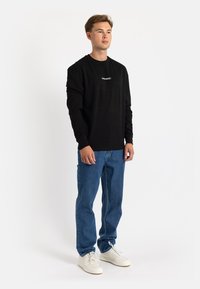 Black long-sleeve t-shirt with text, paired with blue denim jeans and white sneakers. Simple design, cotton material, relaxed fit.