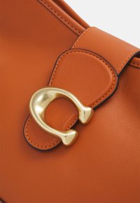 Orangefarbene Lederhandtasche mit einer glatten Textur, goldfarbener Hardware und einem magnetischen Verschluss. Genähte Kanten verleihen Struktur.