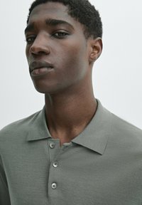 Light gray polo shirt with a collar, three front buttons, and a textured fabric. The fit is close and the material appears smooth.