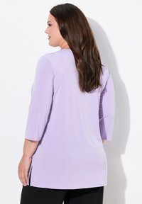 Tunica in lavanda con maniche a tre quarti, texture liscia, fessure sui lati e una vestibilità comoda, progettata per il comfort e la facilità di movimento.