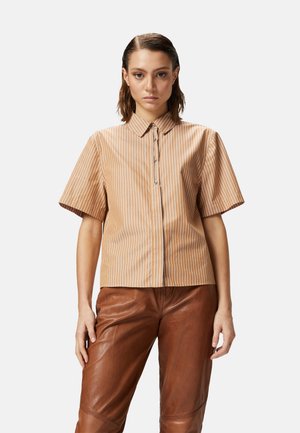 Camicia a maniche corte con colletto di colore marrone chiaro, con righe verticali bianche e chiusura a bottoni, abbinata a pantaloni in pelle marrone.