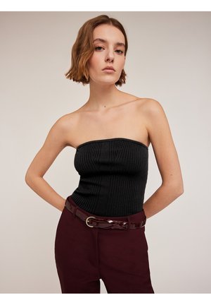 Un top negro sin tirantes de canalé presenta un diseño estructurado, combinado con pantalones de tiro alto en color burdeos asegurados por un cinturón brillante.
