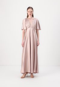 Abito lungo in satin rosa pallido con scollatura a V profonda e maniche svasate, design fluido e leggera lucentezza, abbinato a sandali con tacco beige.