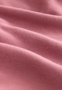 Zachte roze stof met fijne gebreide textuur, voorzichtig gevouwen om een glad en gezellig materiaaloppervlak te tonen.