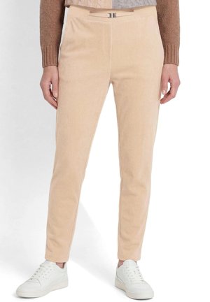 Beige corduroy slim-fit broek gedragen door een persoon met een bruin en grijs gebreide trui en witte sneakers tegen een witte achtergrond.