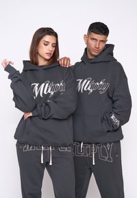 Felpe grigio scuro con grande logo bianco "Multiply". Caratterizzate da una vestibilità oversize, polsini a coste e tasche a marsupio. Abbinati a pantaloni della tuta coordinati.
