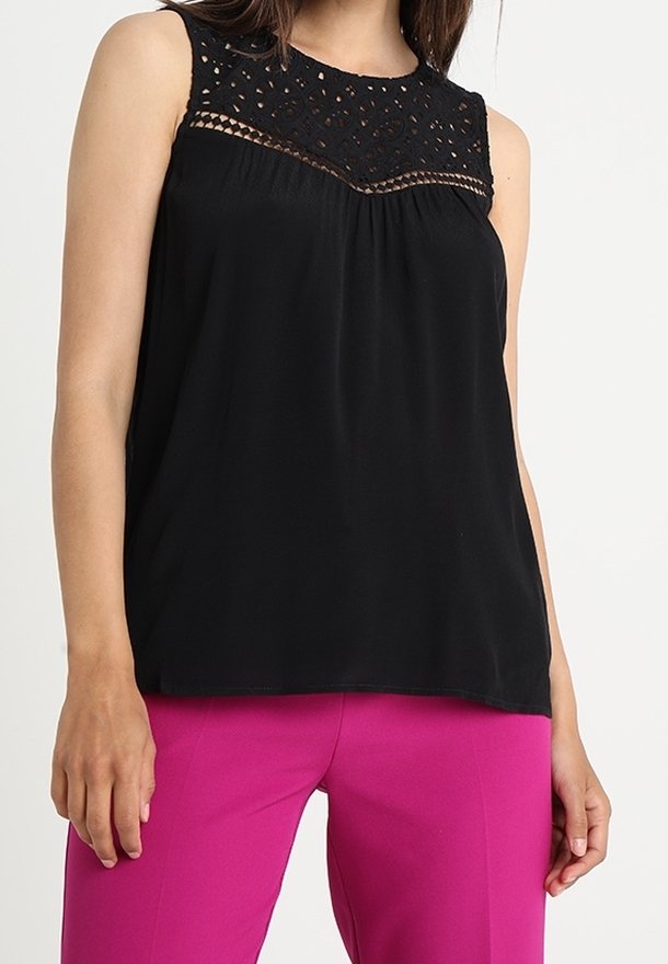 Blouse noire sans manches avec empiècement en dentelle au crochet portée avec un pantalon rose vif sur mesure sur une personne debout.