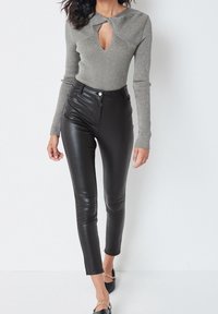 Pull gris côtelé avec une découpe en V au niveau du col et des manches longues, associé à un pantalon skinny taille haute en similicuir noir et des mocassins plats.
