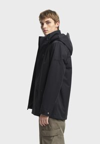Crna vodootporna jakna s kapuljačom, s prednim patentnim zatvaračem, bočnim džepovima i podesivim manžetama. Gladak tekstur i moderan dizajn.