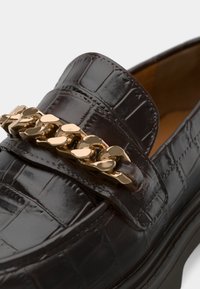 Loafers din piele maro închis cu model de crocodil, accentuați cu o lanț de aur pe pantof; prezintă un design elegant și o suprafață texturată.