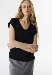 Top corto nero con scollatura a cerchio e aperture laterali, abbinato a pantaloni della tuta grigi. Tessuto morbido e liscio.