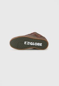 Hnědá a olivová skateboardová bota leží na boku, ukazuje texturovanou podrážku s bílým logem "GLOBE" na spodní části.