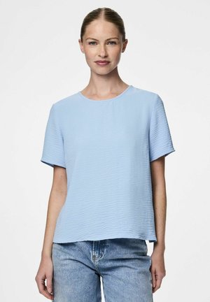 Top à manches courtes de couleur bleu clair avec un motif texturé et ondulé, associé à un jean en denim bleu clair.