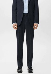 Granatowy garnitur o kroju dopasowanym, z dwurzędową marynarką na dwa guziki, prostymi spodniami oraz błyszczącymi czarnymi butami. Gładka faktura tkaniny.