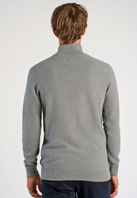 Grauer gestrickter Pullover mit hohem Kragen und gerippten Ärmelbündchen, der ein strukturiertes Muster und seitliche Schlitze am Saum aufweist.