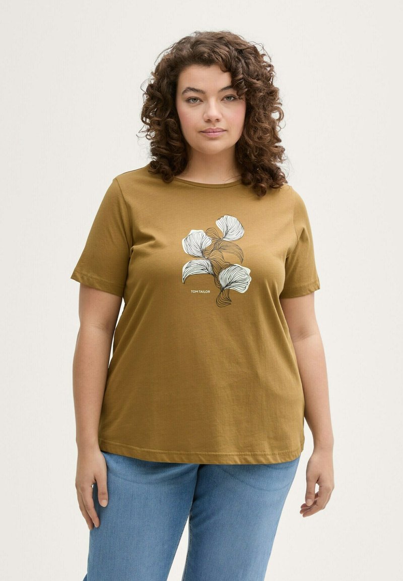 Mosterdkleurig T-shirt van katoen, met een wit lijntekening bloemenontwerp. Korte mouwen en ronde hals. Gecombineerd met blauwe jeans.