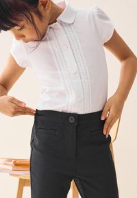 Vit kortärmad blus med knappslå och spetsdetaljer, kombinerad med svarta byxor med framfickor och knappstängning.