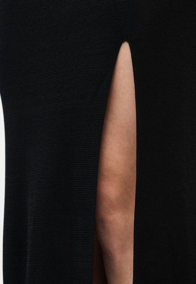 Κοντινό πλάνο σε μαύρη φούστα από ριμπ ύφασμα με κάθετη σχισμή που αποκαλύπτει γυμνό δέρμα από κάτω.