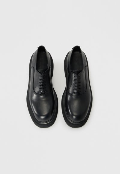 Black leather lace-up shoes with a smooth finish, rounded toe, and thick rubber sole. Features six eyelets and minimalistic design.
