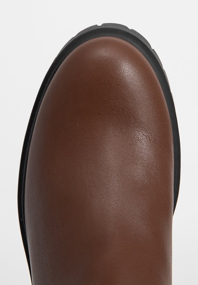 Brauner, glatter Lederstiefel mit schwarzem Gummisohlenschnitt, von oben auf einem weißen Hintergrund fotografiert.