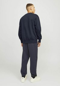 Marine sweatshirt en bijpassende joggingsbroek gemaakt van een zachte stof. De sweatshirt heeft ribbelboorden en een ribbelzoom. Model is van achteren te zien, met witte sneakers aan.
