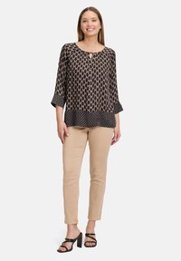 Czarny bluzka w wzory z okrągłym dekoltem, rękawami o długości 3/4, falbaną u dołu; zestawiona z beżowymi spodniami slim-fit i czarnymi sandałami na obcasie.
