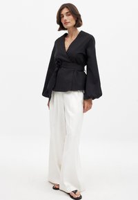 Blusa negra con mangas globo, cintura ceñida y detalle de lazo. Combinada con pantalones anchos blancos y sandalias negras.