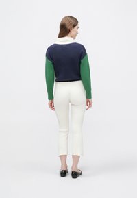 Strikket pullover med navyblå krop og grønne ribstrikkede ærmer, hvid krave, kombineret med cremefarvede ribstrikkede cropped bukser og sorte slip-on sko.